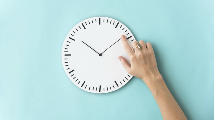 female arm touching white clock against blue background wasting time concept | How to Stop Wasting Time and Get Things Done https://positiveroutines.com/stop-wasting-time/