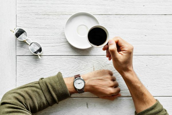 man looking at watch while drinking coffee against white table | How to Stop Wasting Time and Get Things Done https://positiveroutines.com/stop-wasting-time/