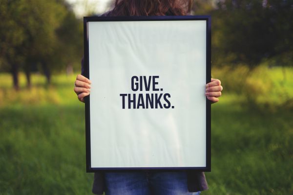 person holding sign that says give thanks against blurry nature background | How to Practice Gratitude With Us This November  https://positiveroutines.com/practice-gratitude/