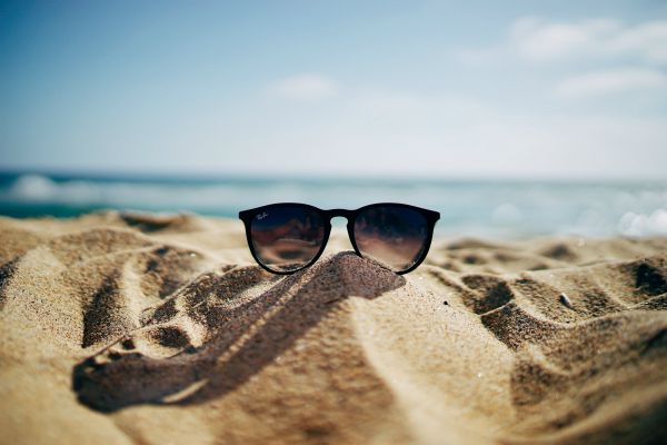 black sunglasses on sand peaks against ocean | The Unmistakable Magic of The 4 Day Week https://positiveroutines.com/four-day-week/