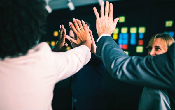 diverse colleagues high fiving | The Unmistakable Magic of The 4 Day Week https://positiveroutines.com/four-day-week/