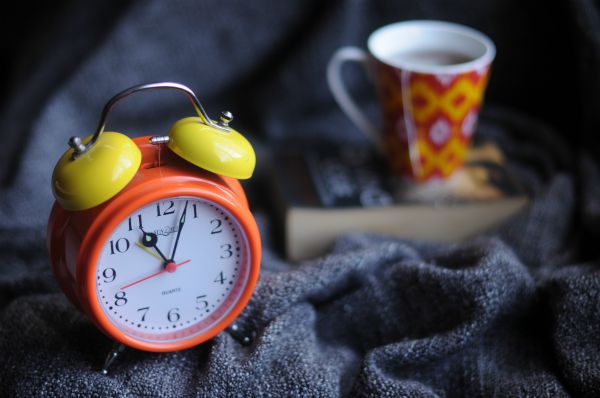 orange alarm clock and coffee mug on blanket | How To Get Focused In The Morning https://positiveroutines.com/get-focused/