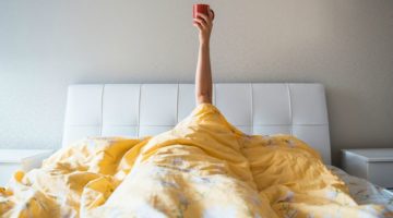 person in bed arm raised holding coffee cup morning | How To Get Focused In The Morning https://positiveroutines.com/get-focused/