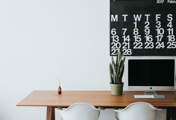 wall calendar over desk with computer and plant | The Unmistakable Magic of The 4 Day Week https://positiveroutines.com/four-day-week/