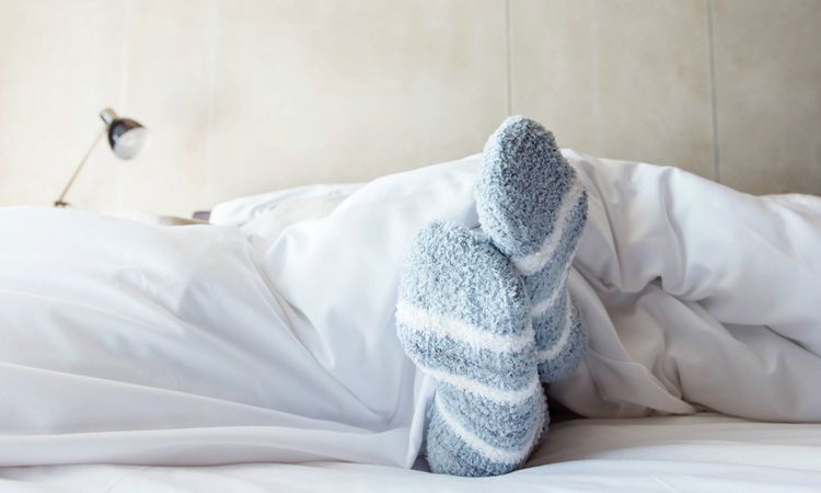 womans feet in winter socks sticking out from under covers | 11 Free Sleep Apps for the Best Nights This Season https://positiveroutines.com/free-sleep-apps/