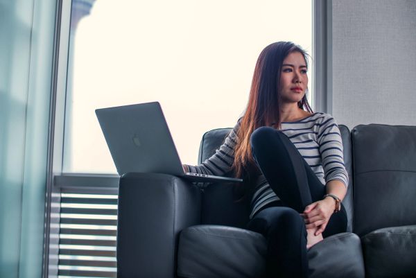 female sitting on couch with laptop looking away in thought | 10 Minutes to Win The Day: How to Set Priorities https://positiveroutines.com/set-priorities/
