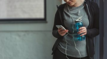 female with headphones using smartphone before workout | The Best Free Workout Apps That Make Exercise Easy https://positiveroutines.com/best-free-workout-apps/