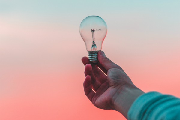 hand holding lightbulb against pastel sunrise | 10 Minutes to Win The Day: How to Set Priorities https://positiveroutines.com/set-priorities/