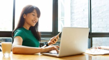 productive woman smiling while using laptop and smartphone | Productive Procrastination Exists. Here's How To Do It. https://positiveroutines.com/productive-procrastination/