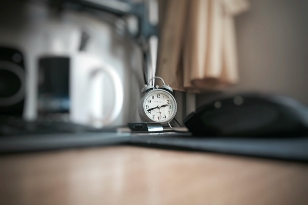 selective focus of grey alarm clock on desk | The Best Tips for Working Remotely When You're Outgoing, Anxious, and More https://positiveroutines.com/tips-for-working-remotely/