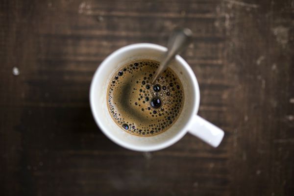 topview mug of fresh coffee on wooden table| The Best Tips for Working Remotely When You're Outgoing, Anxious, and More https://positiveroutines.com/tips-for-working-remotely/
