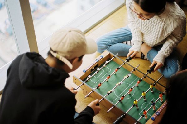 two people sitting on floor playing mini foosball table | The Best Tips for Working Remotely When You're Outgoing, Anxious, and More https://positiveroutines.com/tips-for-working-remotely/