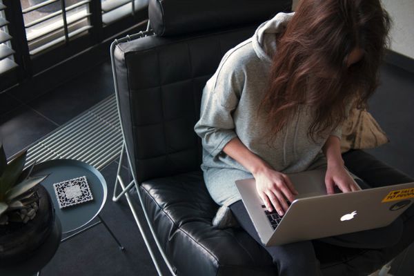 woman working on laptop in leather chair | The Best Tips for Working Remotely When You're Outgoing, Anxious, and More https://positiveroutines.com/tips-for-working-remotely/