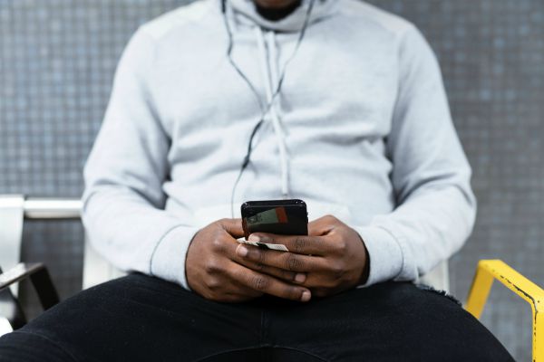 man sitting with phone in hands and earbuds in ears | Make These 5 Tiny Tweaks to Have A Great Morning https://positiveroutines.com/great-morning-tips/