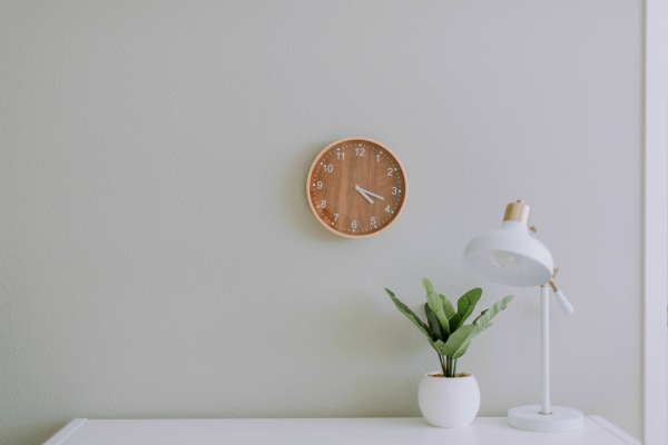 minimalistic desk with wooden clock on white wall | How to Take Advantage of a Flexible Schedule https://positiveroutines.com/flexible-schedule-tips/