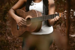 woman-playing-guitar-outdoors | 11 Kind Acts To Brighten Someone's Day https://positiveroutines.com/kind-acts/