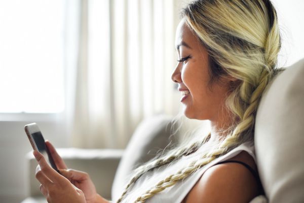 happy woman casually browsing cell phone | An Email Organization Tip for Real People + Why We’re Totally On Board https://positiveroutines.com/email-organization-strategy/