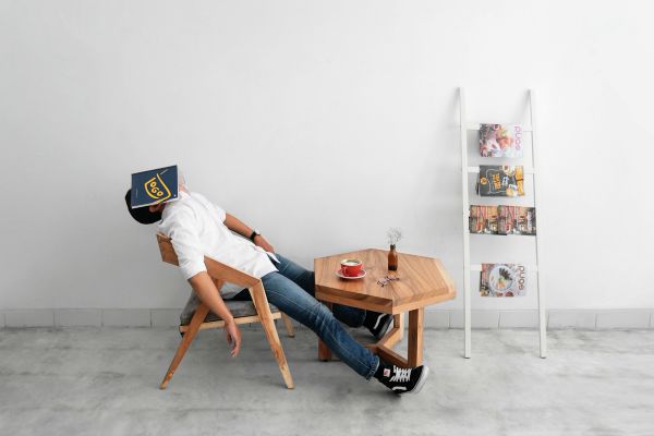 lazy guy slouched in chair covering face with book | What is Procrastination? Causes, Effects, & How to Stop Procrastinating https://positiveroutines.com/what-is-procrastination/