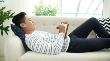 relaxed man on couch writing in gratitude journal | 13 Gratitude Journal Prompts to Try This International Day of Happiness https://positiveroutines.com/gratitude-journal-prompts/