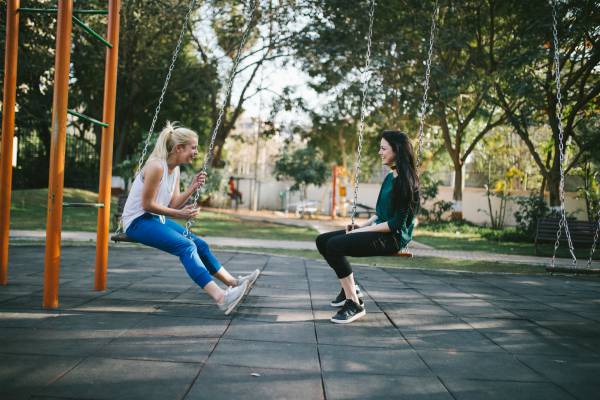 two women swinging and laughing in park | 13 Gratitude Journal Prompts to Try This International Day of Happiness https://positiveroutines.com/gratitude-journal-prompts/