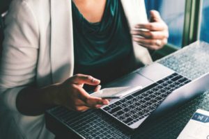 woman using laptop and holding cell phone | An Email Organization Tip for Real People + Why We’re Totally On Board https://positiveroutines.com/email-organization-strategy/