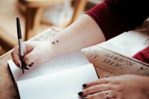 woman writing in journal with black pen | Productivity on Paper: The Happiness Planner vs. Panda Planner https://positiveroutines.com/the-happiness-planner-panda-planner