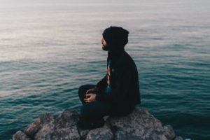 man meditating on rock ledge overlooking ocean | 7 Science-Backed Secrets of a Productive Morning Routine https://positiveroutines.com/productive-morning-routine/