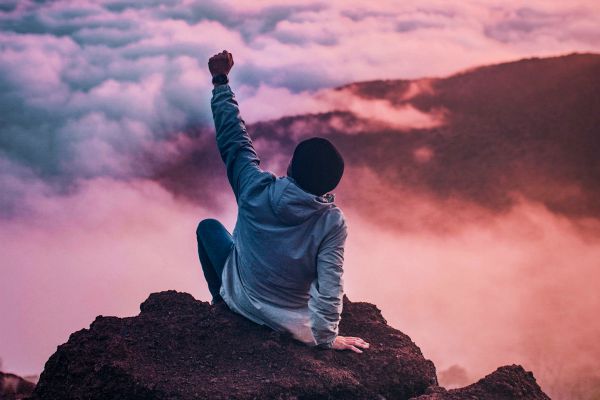 man sitting on cliff in colorful clouds raising fist | What Is Organization? How to Declutter and Organize Your Life https://positiveroutines.com/what-is-organization/