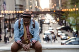 somber man sitting on stone wall overlooking busy traffic | How to Stop Feeling Guilty For Not Getting "Enough" Work Done https://positiveroutines.com/stop-feeling-guilty/