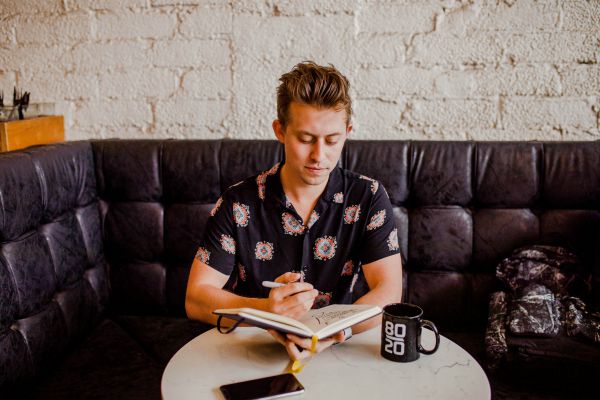 young man sitting with journal and cup of coffee | Productivity on Paper: Best Self Journal vs. Panda Planner  https://positiveroutines.com/best-self-journal-review/
