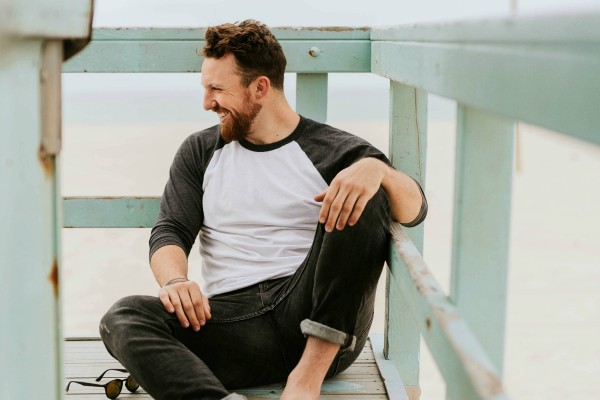 man sitting on beach pier smiling | This is Why We're Happier in Summer https://positiveroutines.com/happier-in-summer