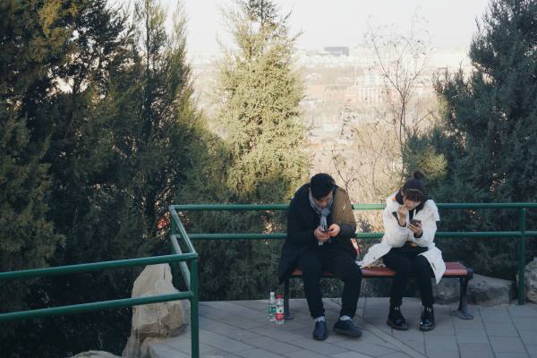 two people sitting on park bench looking at phones | Is Work and Life Balance Even Achievable in 2019? https://positiveroutines.com/work-and-life-balance-tips/