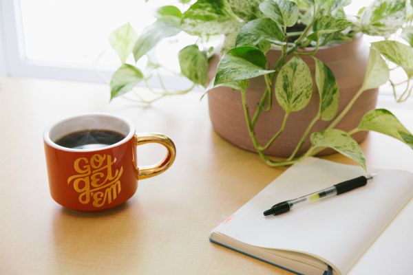 go get em mug and open notebook | 7 Easy Ways to Create a Healthy Work Environment https://positiveroutines.com/work-environment-tips/