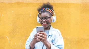 happy woman using headphones and mobile phone | 9 Positive Podcasts For Anyone Who Needs a Mood Boost https://positiveroutines.com/positive-podcasts/