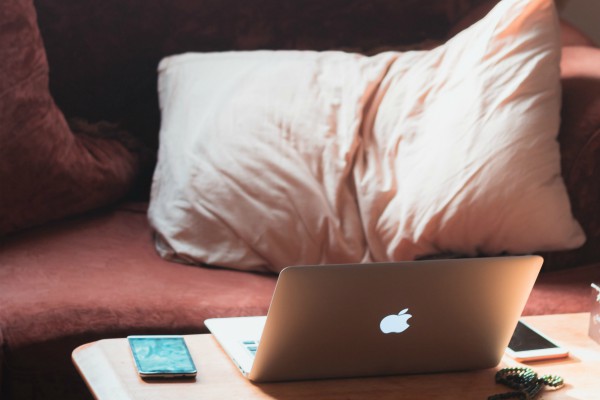 laptop and mobile device on coffee table beside cozy couch and pillows | 7 Sleep Podcasts to Help You Have the Best Rest Ever https://positiveroutines.com/sleep-podcasts/