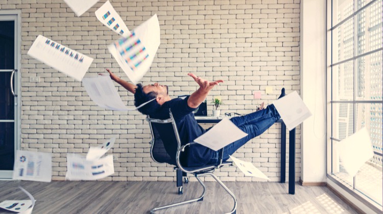 young businessman at desk tossing papers in air at end of work day | How to Leave Work at Work and Actually Enjoy the Weekend https://positiveroutines.com/enjoy-the-weekend/